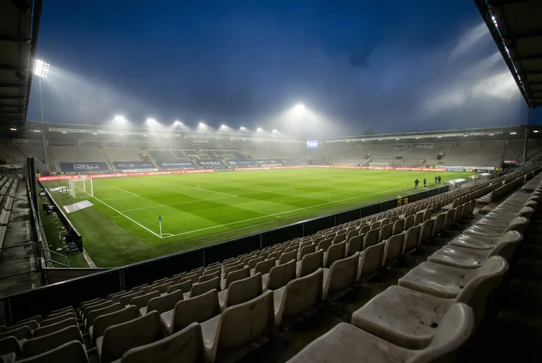 Estádio de futebol visto das arquibancadas com campo verde iluminado durante partida noturna